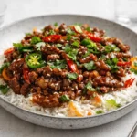 A steaming bowl of Crispy Chilli Beef Rice with spring onions