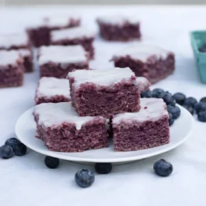 Fudgy Glazed Blueberry Brownies stacked on a wooden table