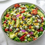 A vibrant Mexican Chopped Salad in a wooden bowl with avocado and charred corn.