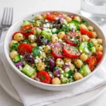 A vibrant Greek Garbanzo Bean Salad in a white bowl on a wooden table.
