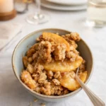 A golden-brown Peach Crisp in a baking dish with melting vanilla ice cream.